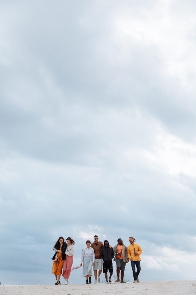 A diverse group of friends enjoys a walk on the beach under a dramatic cloudy sky.